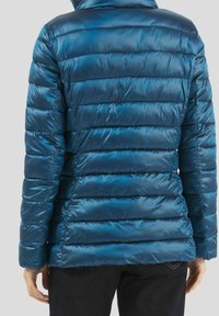 Vatteret jakke i mørkeblå med en skinnende, glat tekstur. Har et vandret quiltet mønster, stående krave og lange ærmer.