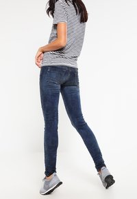 Modré skinny džíny z denimu s vybledlým umyvadlem. V kombinaci s pruhovanou košilí s krátkým rukávem a šedými sportovními botami.