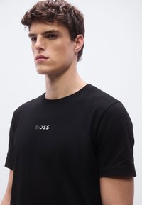 Μαύρο βαμβακερό t-shirt με στρογγυλή λαιμόκοψη και κοντά μανίκια, με ασημένιο κεντημένο λογότυπο «BOSS» στο στήθος. Ομαλή υφή.