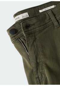 Gros plan sur un pantalon skinny vert avec bouton noir, poche zippée, passant de ceinture et étiquettes de taille indiquant EUR 42 et UK 14.