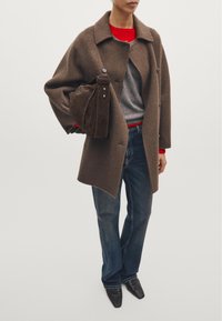 Brown wool overcoat with a structured collar, gray sweater, red accent, blue jeans, and pointed black shoes. Soft texture and tailored design.