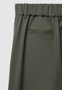 Tessuto verde oliva, testurizzato, con una vita arricciata e passanti per cintura. Presenta un design pulito e sartoriale e una tasca posteriore discreta.