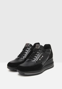 Baskets noires avec une combinaison de cuir brillant et de daim. Les caractéristiques incluent des panneaux texturés, des lacets plats et une semelle compensée rembourrée.