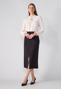 Blusa de tela rosa claro con detalle de lazo, con mangas fruncidas; combinada con una falda lápiz negra hasta la rodilla con una abertura.