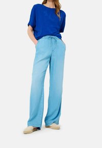 Pantalones anchos de color azul claro con cintura ajustable y dos bolsillos laterales, combinados con una blusa texturizada de color azul royal. Incluye calzado casual.