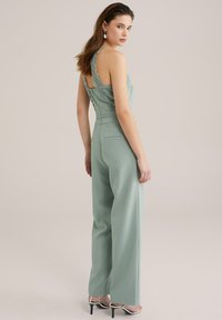 Grön jumpsuit med spetskant på ryggen, vida ben och framfickor. Åtföljs av spetssandaletter med hög klack.