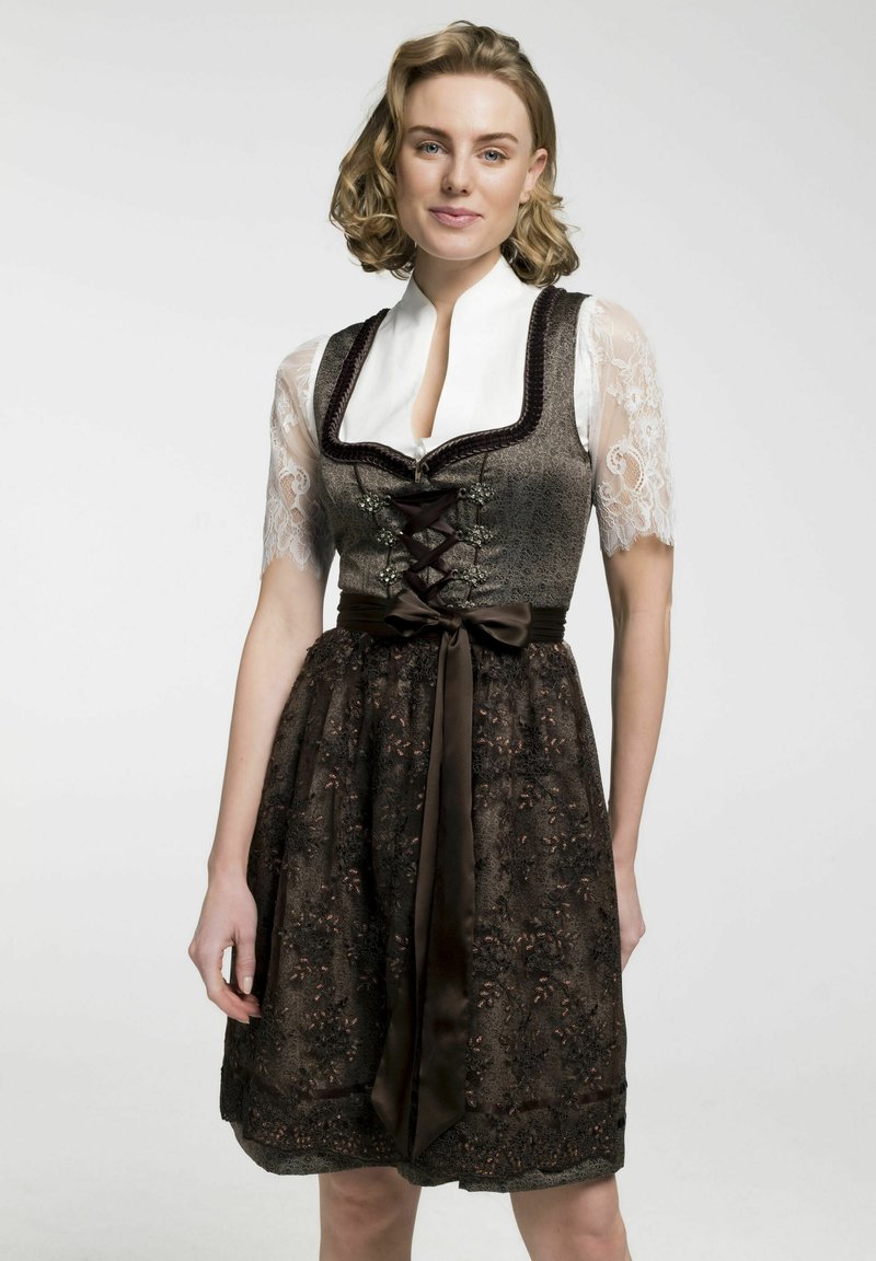 Bruin traditioneel kledingstuk met een kanten blouse, korzetstijl lijfje, decoratieve veters en een satijnen riem. Beschikt over ingewikkelde bloemmotieven.