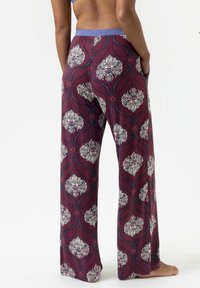 Wijdere broekspijpen in een diep bordeauxrode stof met een bloemenprint in tinten wit, blauw en roze, met een contrasterende tailleband.