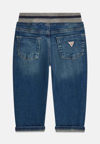 Jean en denim avec une teinte bleu foncé. Dispose d'une ceinture rayée grise et de deux poches arrière avec un patch logo. Détail d'ourlet retroussé.