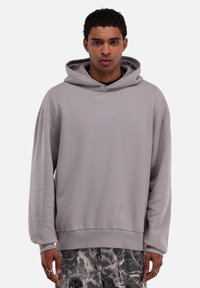 Grauer Hoodie aus weichem Material, mit lässiger Passform, Kordelzugkapuze und kleinem, hellblauen Logo auf der Brust.