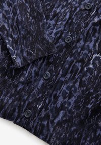 Cardigan en tricot avec un motif abstrait bleu foncé et noir. Il possède un col et des poignets côtelés avec des boutons en plastique noir.