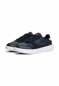Sneaker da uomo blu navy a bassa altezza con suole bianche, design con lacci, etichetta rossa sulla linguetta e marchio Tommy Hilfiger sul lato.