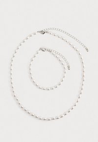 Colar de pérolas e pulseira correspondente com fechos de corrente de prata dispostos sobre um fundo branco.