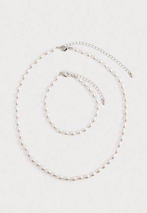 Gyöngy nyaklánc és hozzáillő karkötő ezüst lánc kapoccsal, fehér háttérre elhelyezve.