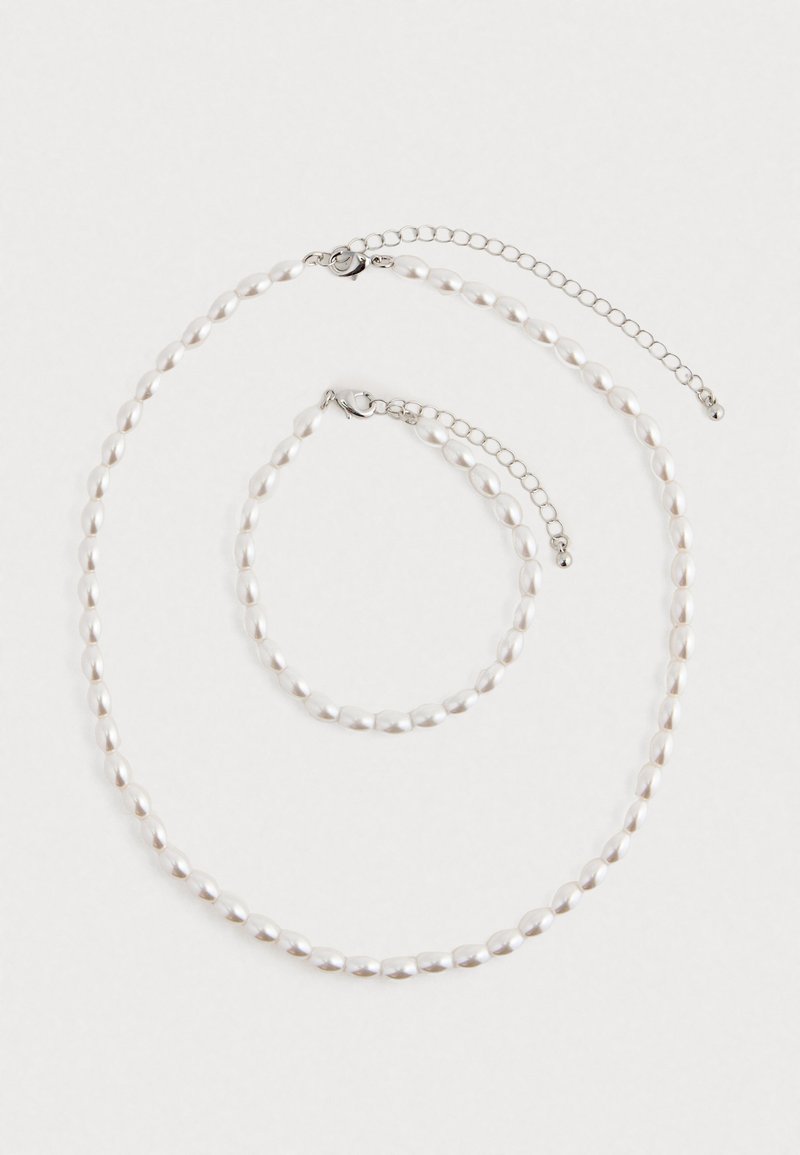 Colar de pérolas e pulseira correspondente com fechos de corrente de prata dispostos sobre um fundo branco.