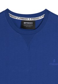 Camicia in cotone blu con scollo a girocollo, caratterizzata da un accento a forma di V sul colletto e un piccolo logo sul davanti.