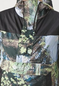 Giacca multicolore resistente alle intemperie con una sezione superiore nera e una sezione inferiore decorata con accenti verdi e blu. Logo Columbia visibile.