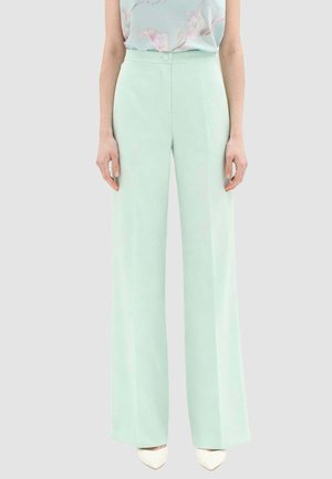 Donna con pantaloni a vita alta, gamba larga di colore verde menta abbinati a una canotta floreale pastello e scarpe bianche con punta appuntita.