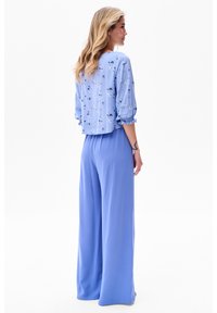 Helles blaues Blusenshirt mit floralen Mustern und puffärmeln, kombiniert mit locker sitzenden hellblauen Hosen. Weiche Textur, entspanntes Design.