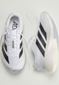  Paire de chaussures de course Adidas Adizero blanches avec des bandes noires et des lacets blancs défaits sur un fond clair.