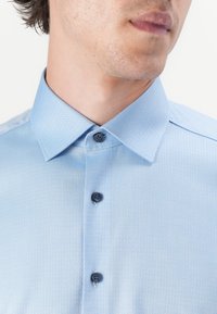 Himmelblaues Hemd mit strukturiertem Muster, spitzem Kragen und schwarzen Knöpfen. Bietet ein gepflegtes Design mit glattem Stoffabschluss.