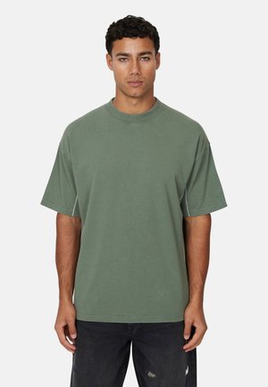 Cotton oversized green t-shirt with a round neck, short sleeves, and contrasting stitching. Paired with distressed dark jeans.