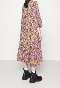 Blommig midiklänning med mönster i lila, gult och rosa; lös passform och utsvängd nederkant. Svarta kraftiga ankelskot som har sidopaneler i botten.
