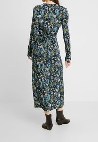 Långärmad maxiklänning i mörk marinblå med livfulla blommönster i turkos och grön. Har en knytning i midjan och en texturerad tyg.