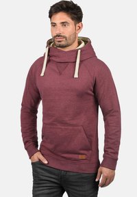 Burgundy pullover hoodie with a cowl neck, drawstrings, and front pocket. Features a textured fabric and contrasting inner lining.