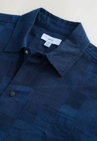 Chemise à manches courtes à carreaux navy en tissu texturé avec col boutonné et une poche poitrine.