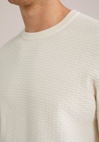 Helles beige, strukturiertes Strickoberteil mit einem runden, gerippten Kragen und einem Rautenmuster auf dem Stoff. Keine sichtbaren Logos oder Verzierungen.