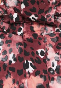 Gros plan d'une doudoune grenat avec des taches léopard irrégulières noires et blanches et un bouton rond grenat embossé du mot "ROXY."