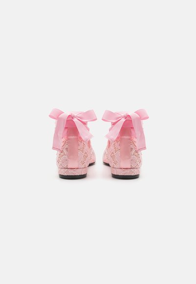Zapatos rosa con cordones, con un exterior de encaje texturizado, lazos de cinta de satén rosa a juego en la parte trasera y una suela negra para el contraste.