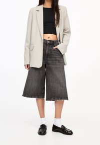 Jasnoszary żakiet, czarny krótki top, ciemnoniebieskie kuloty o wysokim stanie z postrzępionym dołem, czarne loafersy i białe skarpetki sięgające kostek.