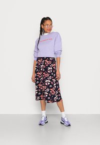Sweatshirt lilás claro com a imprensa "STAY SIMPLE & TRUE", saia midi floral azul-marinho e ténis roxos com detalhes brancos.