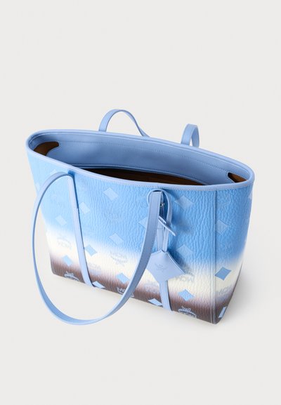 Τσάντα ώμου με διαβαθμισμένα μπλε και λευκά χρώματα και μοτίβο με μονόγραμμα, δύο λουριά για τον ώμο και ανοιχτό πάνω μέρος που αποκαλύπτει καφέ εσωτερική επένδυση.