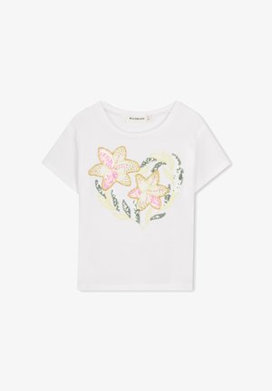 Wit katoenen T-shirt met een hartvormig ontwerp met twee bloemen in roze, geel en groene pailletten, omringd door groene bladeren.