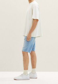 Camiseta oversized gris claro, pantalones cortos de mezclilla azules, zapatillas blancas, calcetines de color claro. Ajuste casual, mangas cortas, pantalones cortos hasta la rodilla.