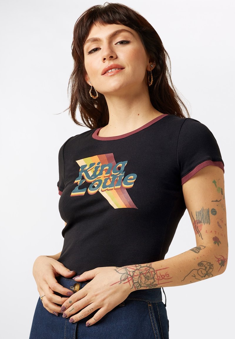 T-shirt noire ajustée avec un col côtelé bordeaux. Présente un graphique rétro coloré "King Louie" avec des rayures horizontales.