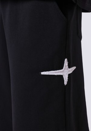 Tessuto nero con una toppa bianca ricamata a forma di stella vicino alla cucitura della tasca sul lato di un indumento.