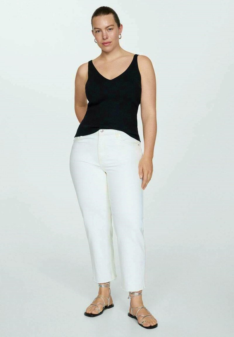 Czarny prążkowany top na ramiączkach z wycięciem w serek, w zestawie z białymi, krótkimi dżinsami i płaskimi sandałami na paski. Modelka stoi z luzem, z rękami wzdłuż ciała.