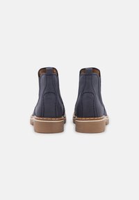 Stivali alla caviglia in pelle blu navy con texture liscia, pannelli elastici laterali, suola marrone a contrasto e dettagli di cucitura lungo le cuciture.