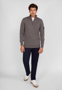 Pulover gri cu mânecă lungă și guler cu fermoar, purtat peste o cămașă albă, asortat cu pantaloni negri și adidași albi.