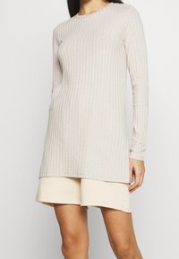 Beżowa prążkowana tunika z długim rękawem, okrągłym dekoltem, dopasowanym krojem i bocznymi rozcięciami, zestawiona z jasnobeżowymi szortami.