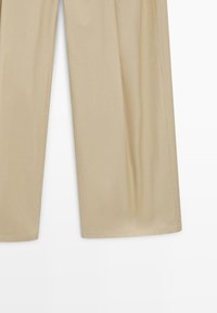 Beige Weitbein-Hose mit glatter Textur, sichtbaren Nähten entlang der Nähte, vor einem weißen Hintergrund präsentiert.