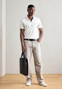 Hvid polo shirt med lynlås krave, lysegrå denim jeans, sort læder tote bag og hvide sneakers med røde detaljer.