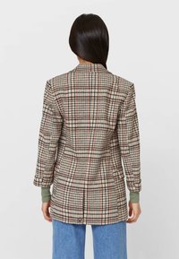 Blazer a quadri con motivo check beige, rosso e blu navy, spalline e polsini a coste verdi. Vestibilità su misura con spacco posteriore singolo.