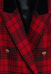 Rot-schwarz kariertes Doppelreihensakko mit goldenen Knöpfen und einem schwarzen Samt-Revers. Strukturierter Stoff mit markantem Karomuster.