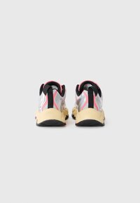 Sportliche Schuhe mit einem Obermaterial aus silbernem Mesh, pinken Akzenten und einem schwarzen Fersenbereich; klobige gelbe Gummisohle; reflektierende Details an den Seiten.