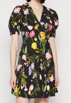 Robe courte noire à fleurs avec manches bouffantes, ornée de fleurs roses, jaunes, orange et violettes, portée par une personne avec un tatouage d'ancre sur le bras.